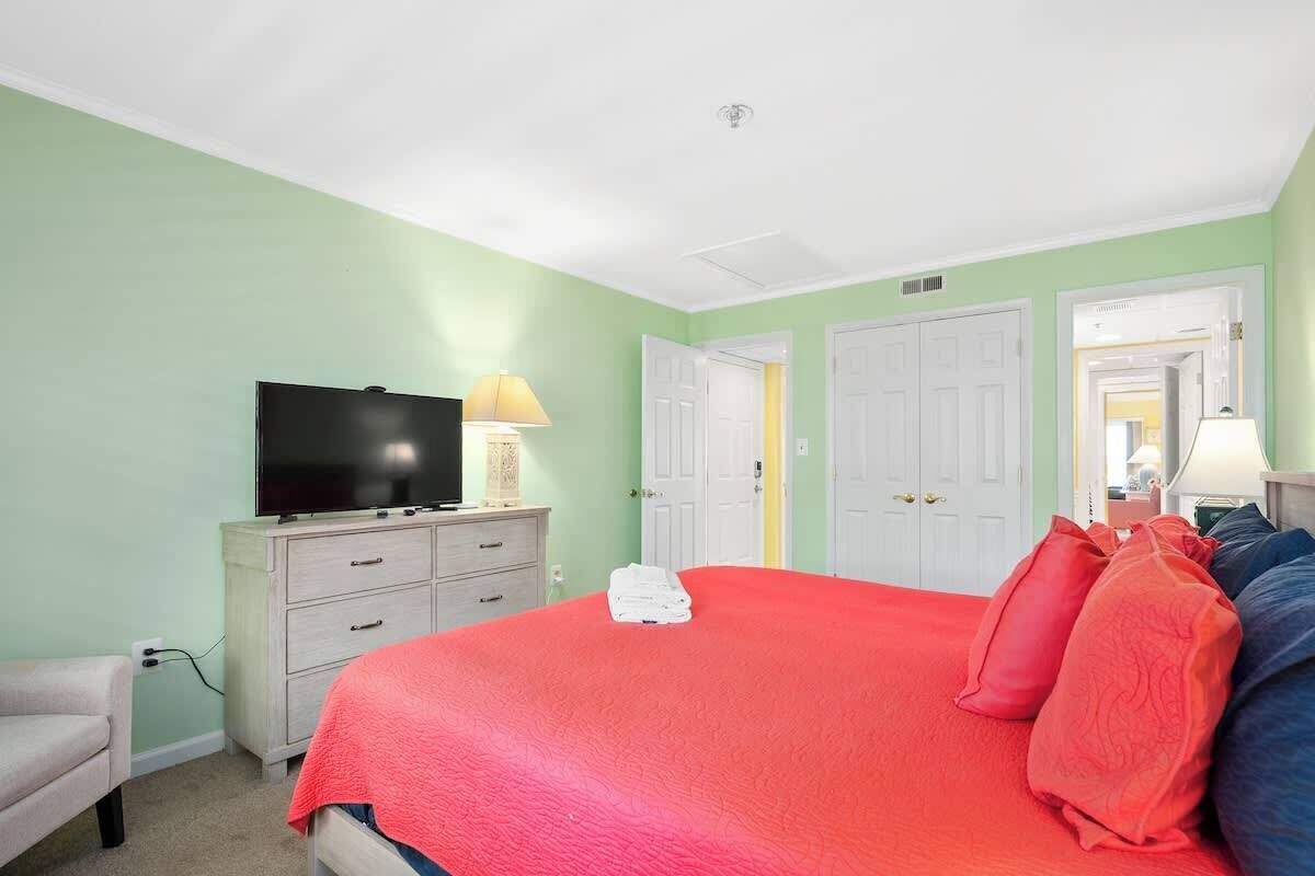 A bedroom with a large bed, a television on a dresser, and a door leading to another room.