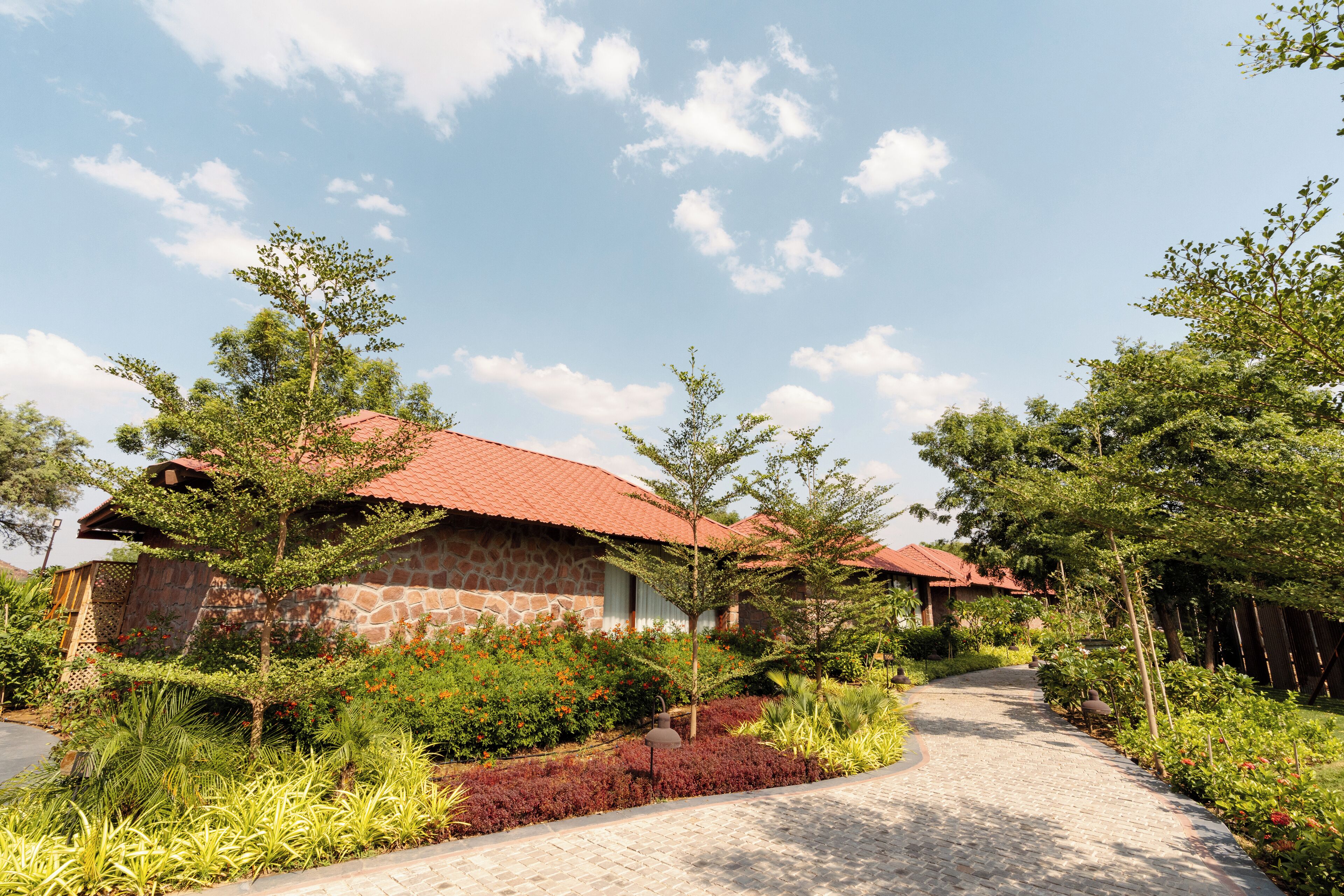 A stone building with a red roof, surrounded by lush greenery and a paved pathway.