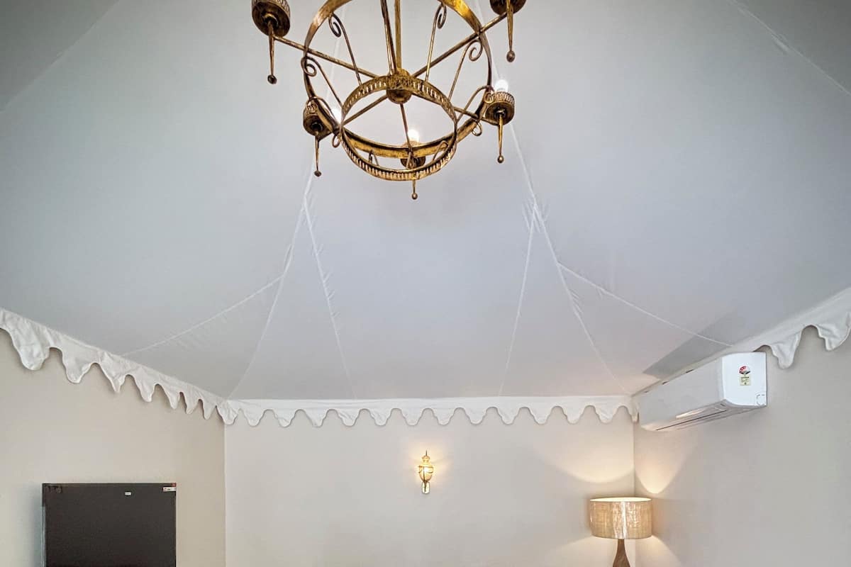 Een gezellige kamer met een bruine bank, twee fauteuils, een houten salontafel, een kroonluchter, een flatscreen televisie, een lamp en een plafondventilator.