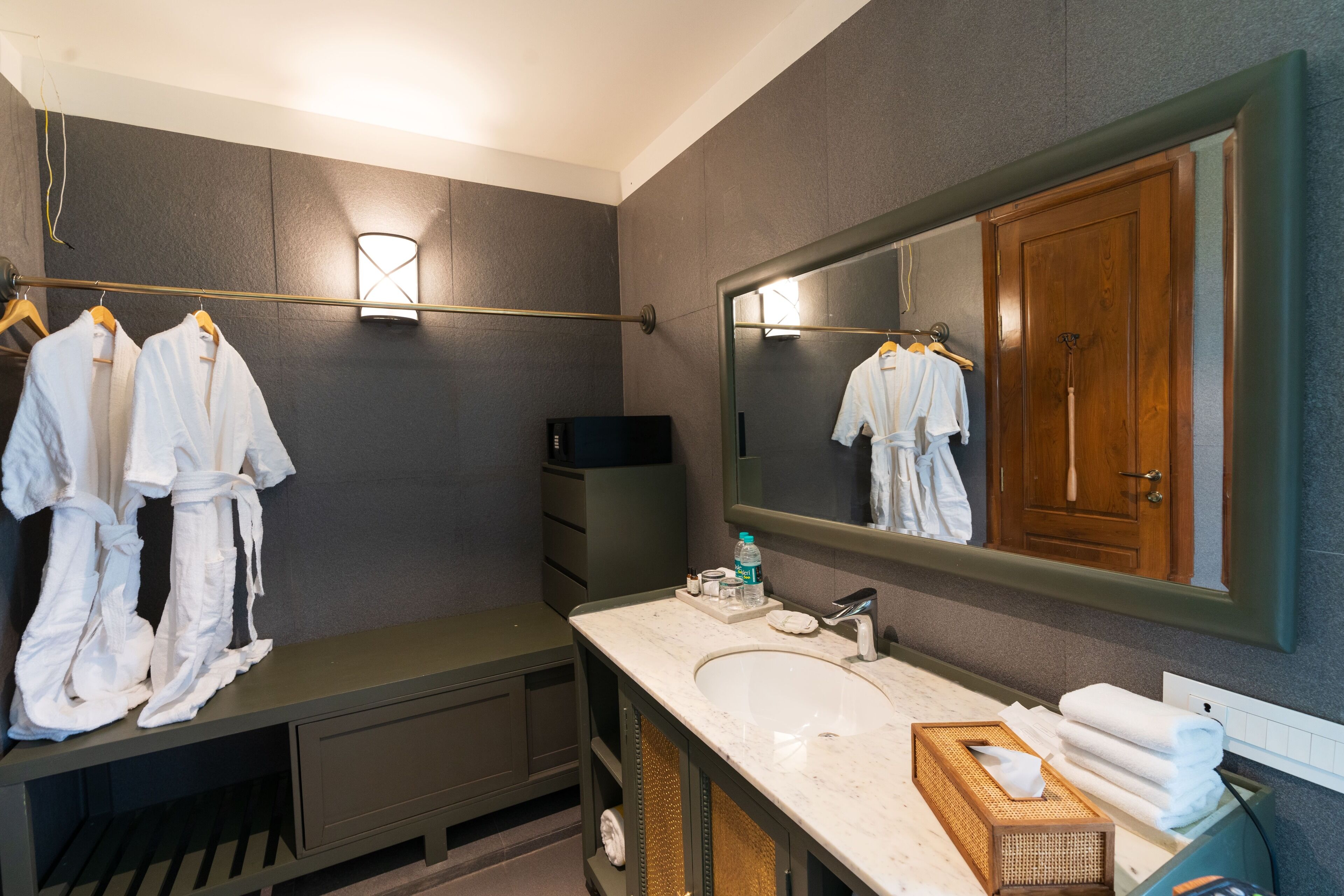 Un baño moderno con un espejo grande, un lavabo y tocador. Toallas y albornoces cuelgan en un perchero.