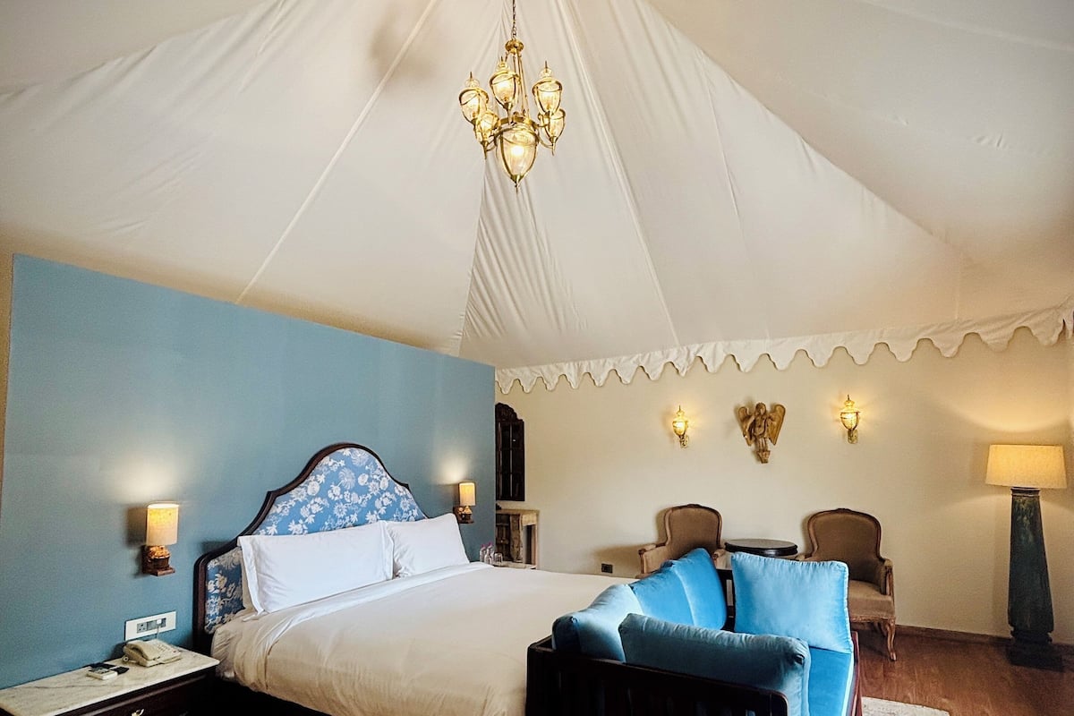 Een slaapkamer met een groot bed, een kroonluchter, een nachtkastje, een stoel en een lamp.