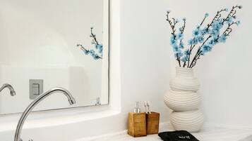 Un baño con lavamanos blanco, un espejo y un florero con ramas.