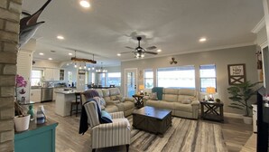 A spacious living room with a sofa, armchairs, and a coffee table. There is a kitchen in the background with a dining area. - Hidden Gem Waterfront home in gated Country Club community on Lake Conroe.   (Montgomery)