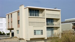 Un edificio moderno de dos pisos con balcones, techo plano y suelo arenoso.