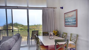 Un comedor con mesa, sillas y vista a la playa a través de amplias ventanas.
