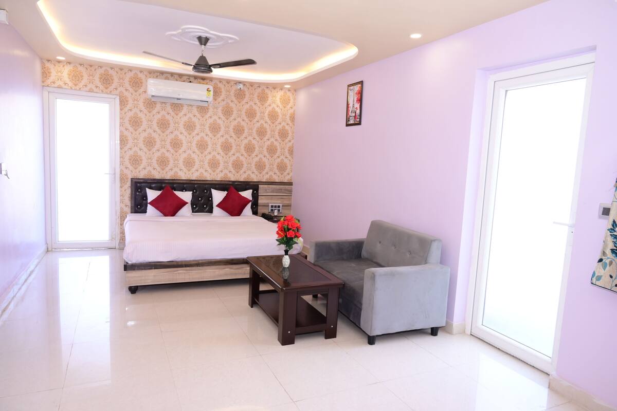Une chambre à coucher comprenant un lit, un canapé, une petite table avec un vase, un ventilateur de plafond et une fenêtre.