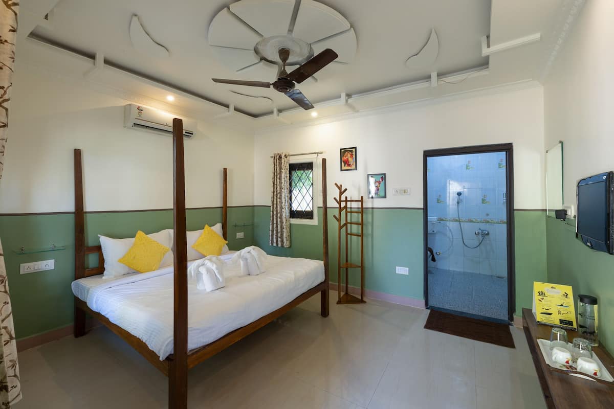 A four-poster bed with white linens and yellow pillows, a ceiling fan, a shower area, and a wooden ladder.