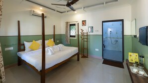 A four-poster bed with white linens and yellow pillows, a ceiling fan, a shower area, and a small table with glasses and a tray. - Avadale Tadoba - Stag Groups Not Allowed (Bhadravathi)