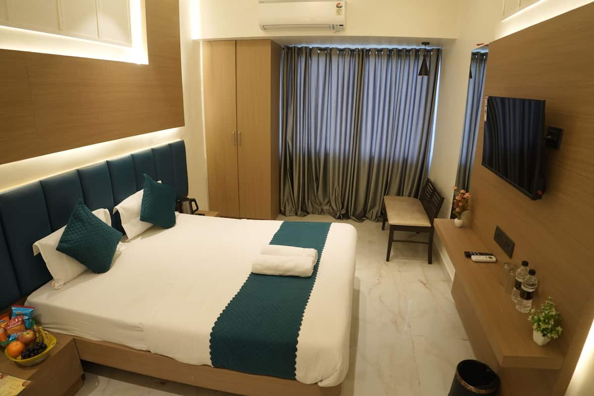A hotel room with a bed, a desk, a chair, a small table, an air conditioning unit, a curtain, a mirror, and a reception desk.