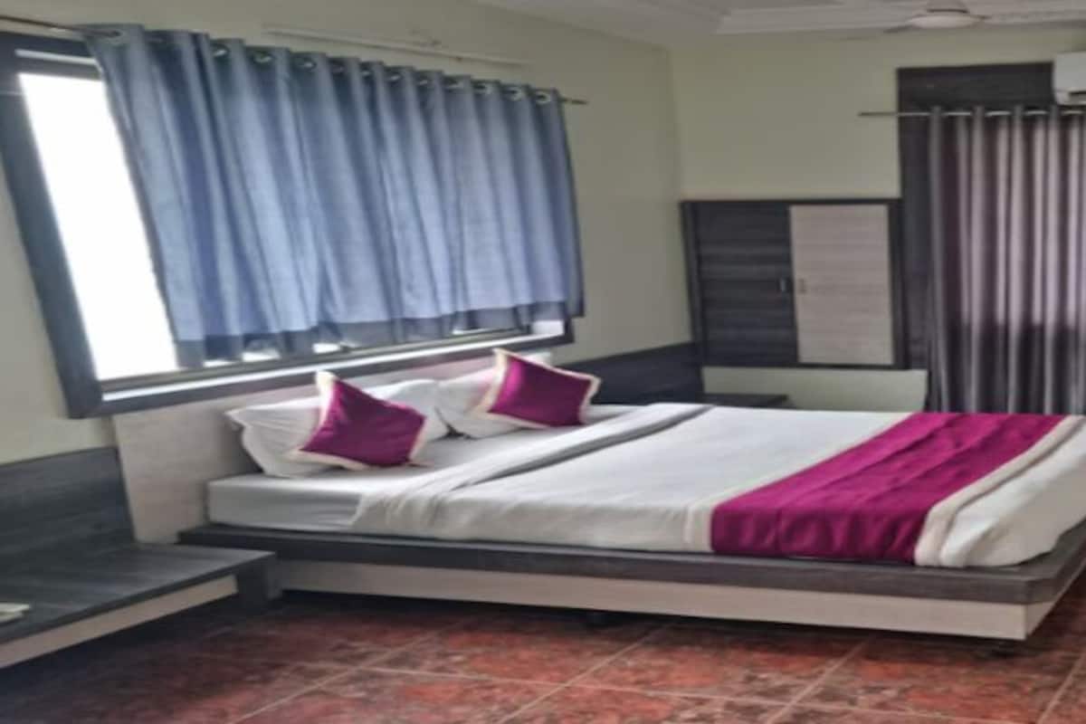 A hotel room with a bed, curtains, an air conditioning unit, a television, and a small table.