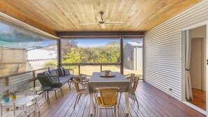 A covered outdoor patio with a table and chairs, a sofa, and a view of a residential area. - Swell Times Holiday Home - Busselton (West Busselton)
