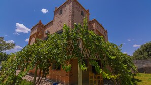 A traditional building with a symmetrical facade, multiple windows, and a stone wall in the background. - Kasbah Roseville  (Ait Sedrate Sahl El Gharbia)