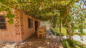 A covered outdoor area with a patterned wall, a wooden bench, and a pathway. - Kasbah Roseville  (Ait Sedrate Sahl El Gharbia)