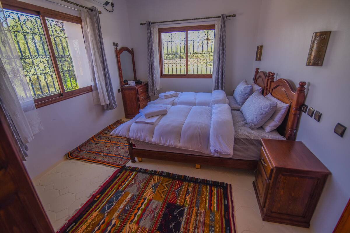 Une chambre à coucher avec un grand lit, une table de chevet en bois, une commode et une fenêtre avec des rideaux.