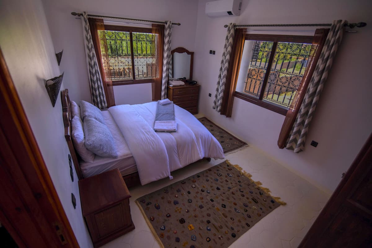 Une chambre à coucher avec un lit, une commode et deux fenêtres avec des rideaux.