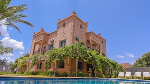 A large building with a pool in front, surrounded by greenery and a clear blue sky. - Kasbah Roseville  (Ait Sedrate Sahl El Gharbia)