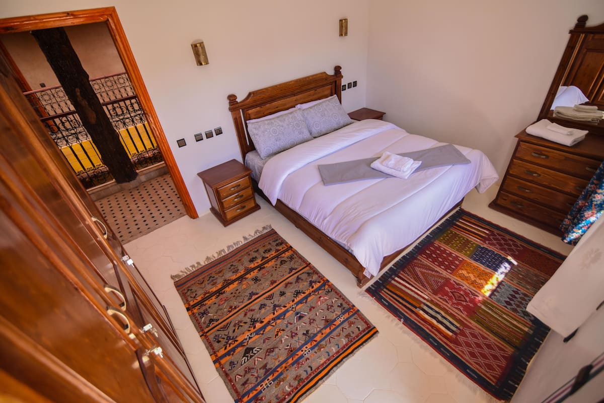 Une chambre à coucher avec un lit en bois, deux tables de chevet, une commode et un grand tapis à motifs.