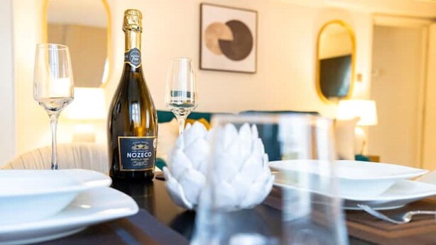 A dining table set with a bottle of Nozéco champagne, two glasses, and a white floral centerpiece. - Hidden Gem in Covent Garden, contemporary design with private terrace (London)