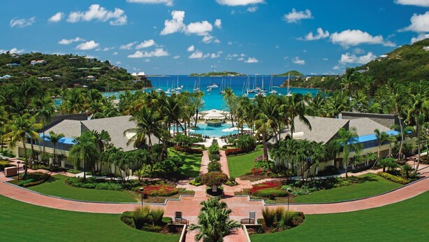 A resort with a central pool, palm trees, and a view of the ocean.