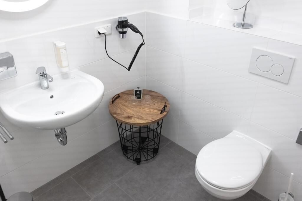 Une salle de bain moderne avec un lavabo blanc, des toilettes et une table ronde en bois dotée d’un cadre en métal.