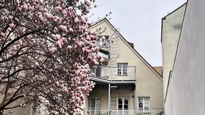 A courtyard with a two-story building, a tree with pink blossoms, and outdoor seating. - ANA Suites Augsburg City Center (Augsburg)