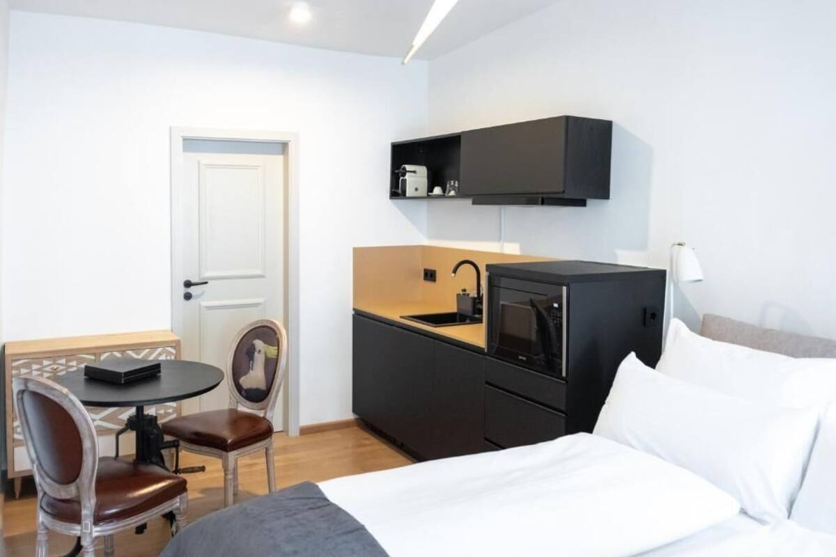 A compact hotel room with a bed, a small dining table with chairs, a kitchenette with a microwave, and a white door.