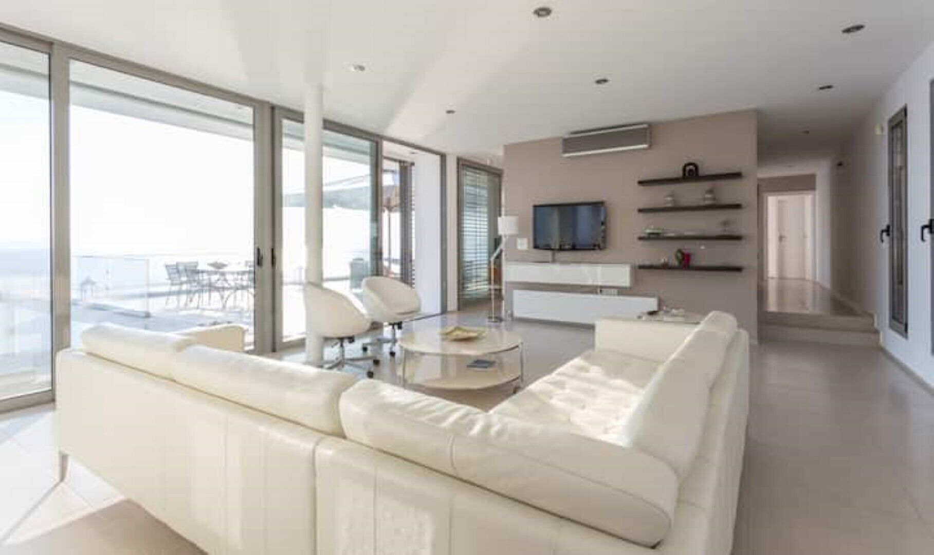A modern living room with a white sofa, a glass coffee table, and a TV on a white cabinet.