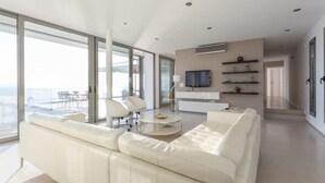 Una sala de estar moderna con un sofá blanco, una mesa de centro de vidrio y un televisor sobre un mueble blanco.