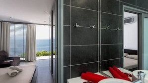 Un baño moderno con un espejo grande, paredes cubiertas de azulejos oscuros y vistas al mar.