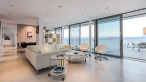 Una sala de estar moderna con un sofá blanco, una mesa de centro y una silla, con ventanas amplias que ofrecen vistas al mar.