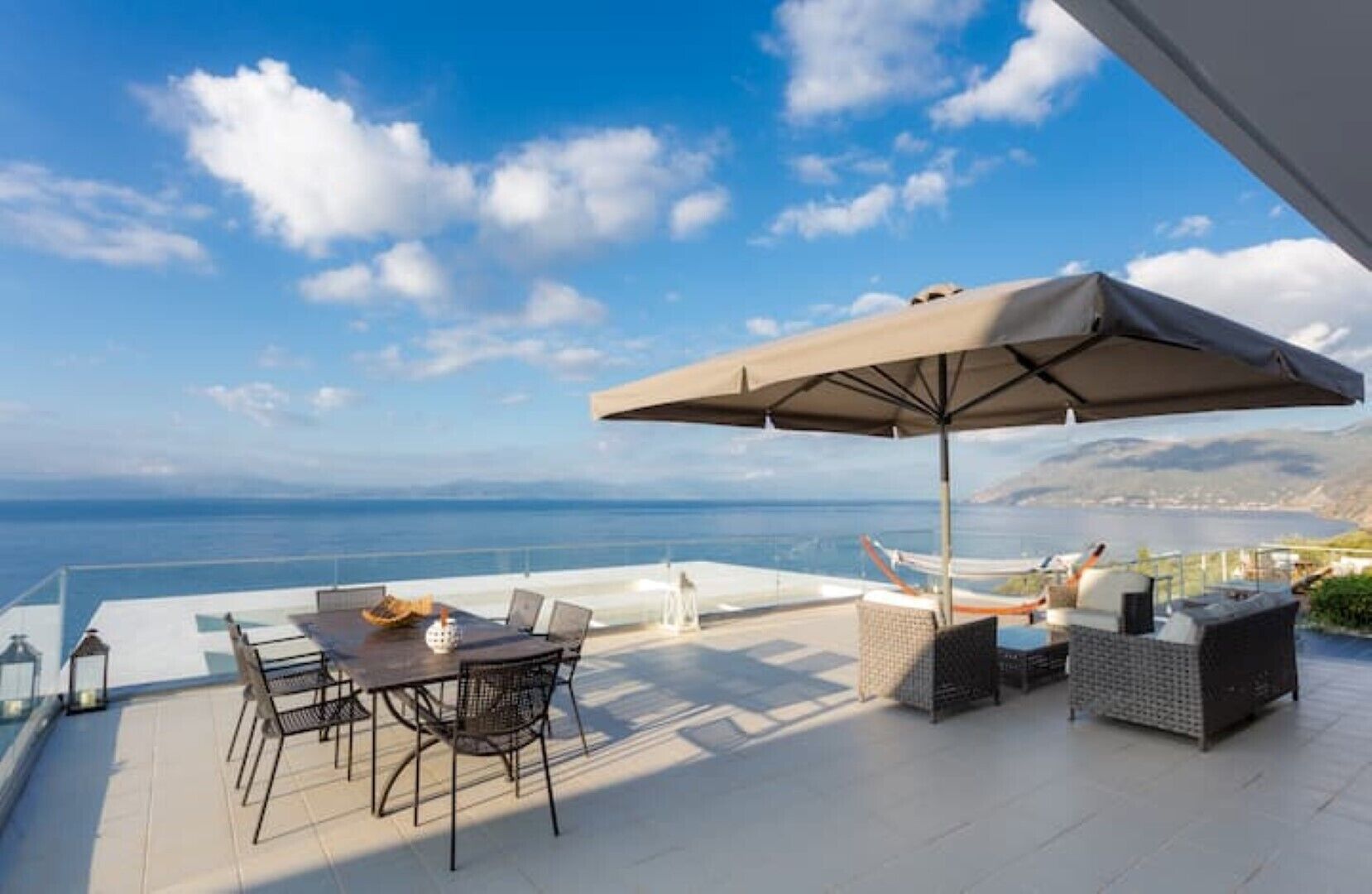 A terrace with a table and chairs, a large umbrella, and a view of the sea.