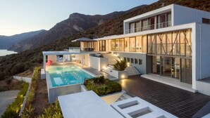 Una casa moderna de dos pisos con piscina, amplias ventanas y vista al mar.