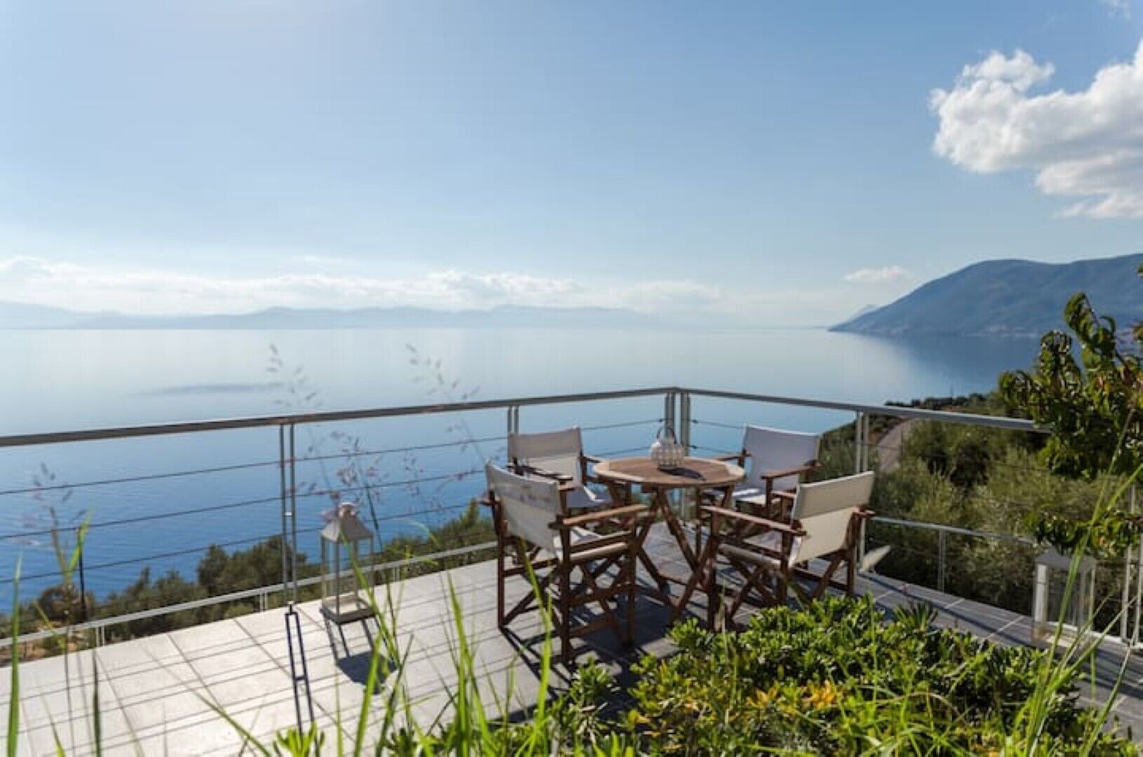 Een terras met tafel en stoelen met uitzicht op een prachtig zee- en berglandschap.
