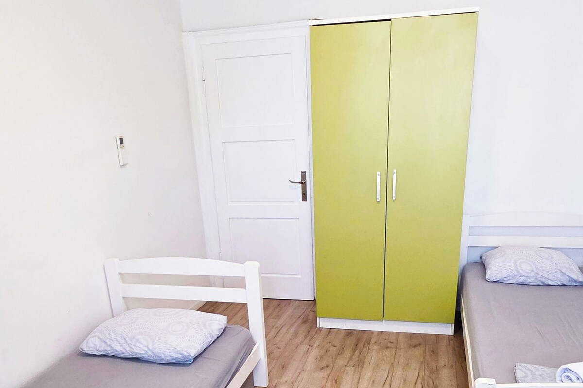 A room with two single beds, a green wardrobe, and a white door.