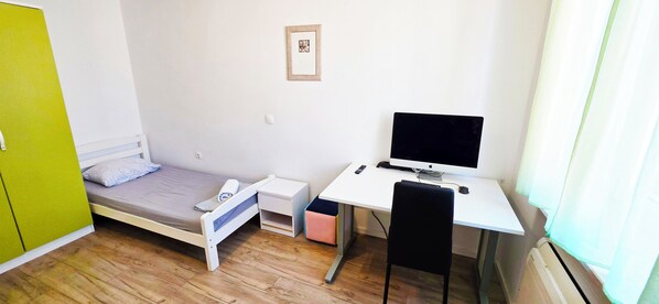 A small, single-room accommodation with a bed, a desk with a computer, a chair, and a heater. - Chillax Rooms (Split)