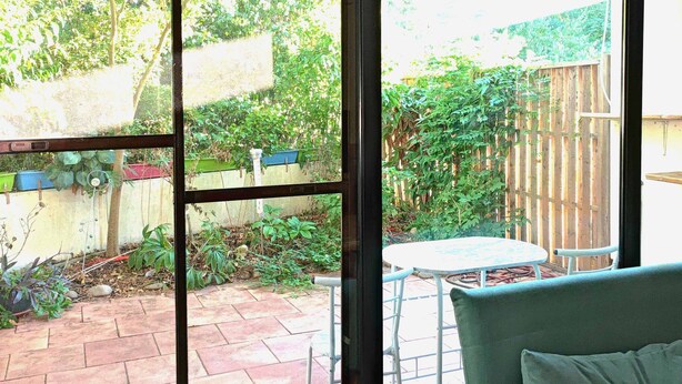 A room with a large sliding glass door leading to a patio with a table and chairs, a wooden deck, and a garden. - Wunderschönes Apartment Ob12-e mit Terrasse in Mainz (Mainz)