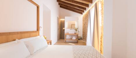 Una habitación de hotel moderna con una cama grande, vigas de madera en el techo, un baño con espejo y un edredón estampado sobre la cama.