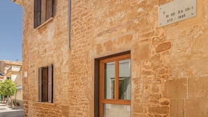 A stone building with a wooden door and shutters, a sign with a date, and a paved street. - Petit Palau Alcudia Boutique Hotel (Alcúdia)