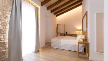 A bedroom with a bed, a bedside table with a lamp, a mirror, and a stone wall.