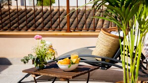A patio with a table set with a bowl of fruit and a glass of orange juice, a wicker basket, and a potted plant. - Petit Palau Alcudia Boutique Hotel (Alcúdia)