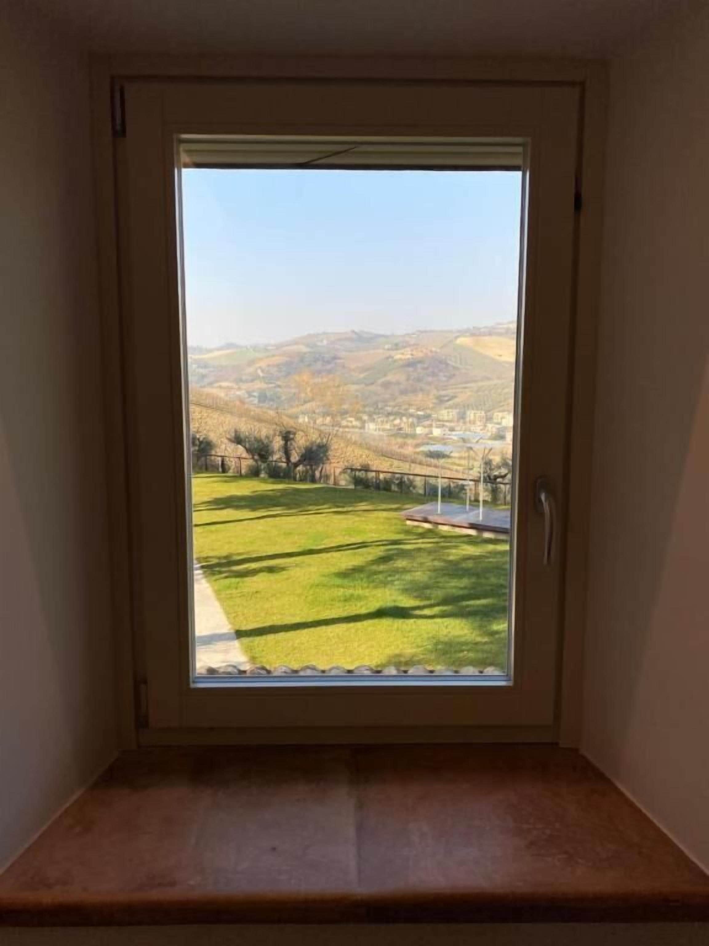 Een kamer met een raam dat uitkijkt over een grasveld en heuvels in de verte.