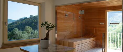 Un baño moderno con sauna de vidrio, vista al bosque y una mesa de mármol con planta en maceta.