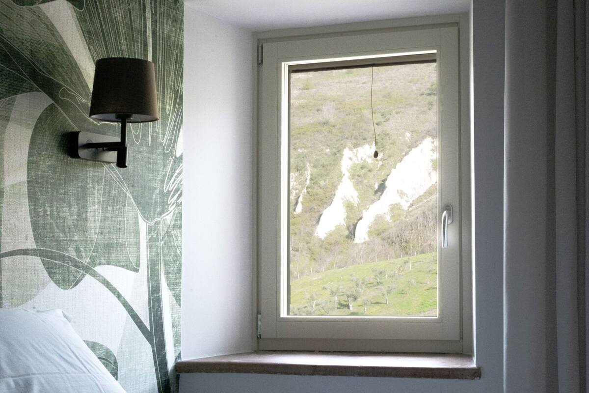 A bedroom with a bed, a nightstand, a lamp, and a window with a view of a landscape.
