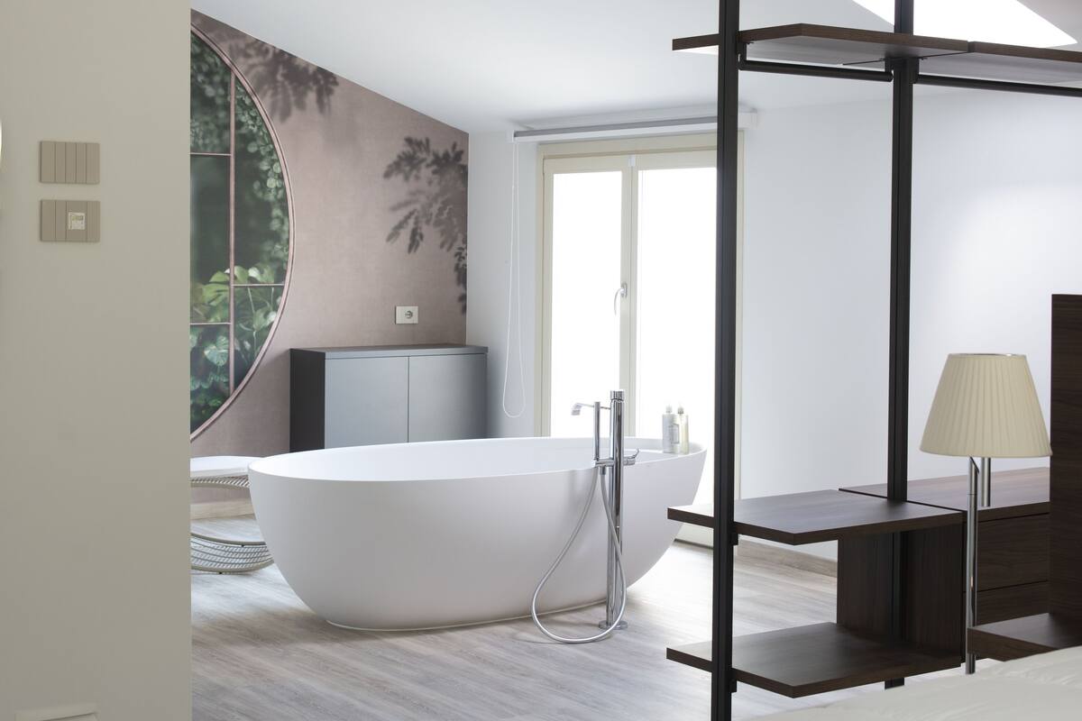 A modern bedroom with a large bed, a bathtub, a desk, and a large window.
