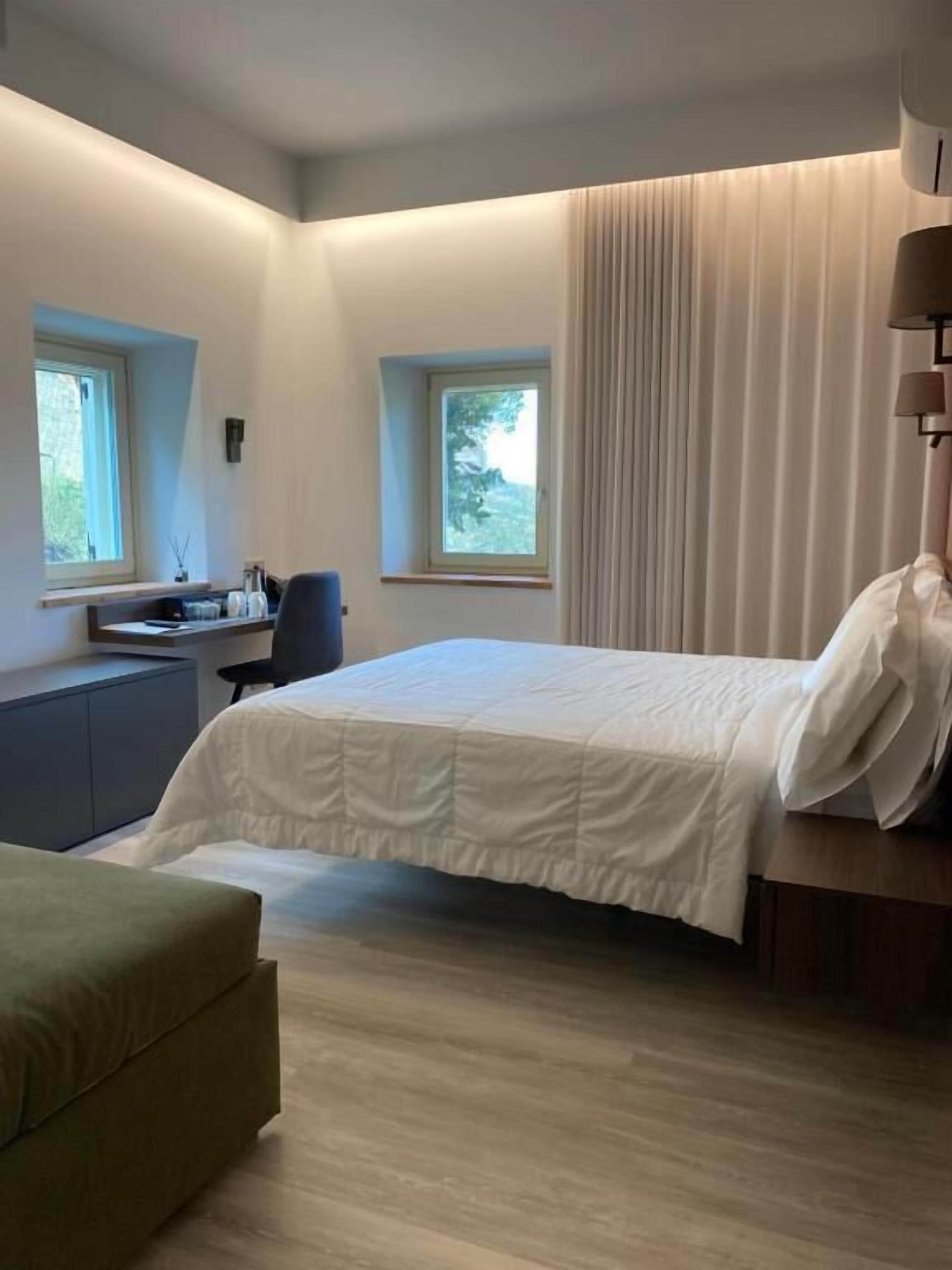 Une chambre moderne avec un lit, un bureau et une chaise. Deux fenêtres laissent entrer la lumière naturelle.