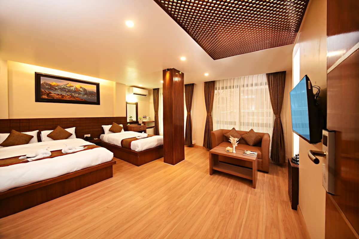 A hotel room with two beds, a sofa, a TV, and a wooden floor.