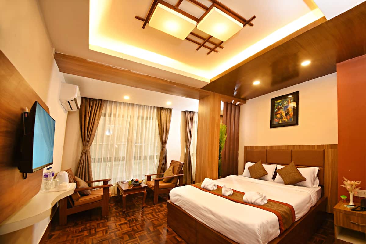 A hotel room with a large bed, a desk with a chair, a TV, and a window with curtains.