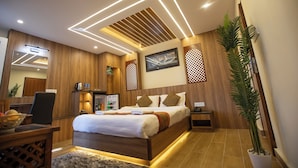 A modern hotel room with a wooden bed, a desk with a chair, a small refrigerator, and a potted plant. - Capital Boutique Hotel (Kathmandu)