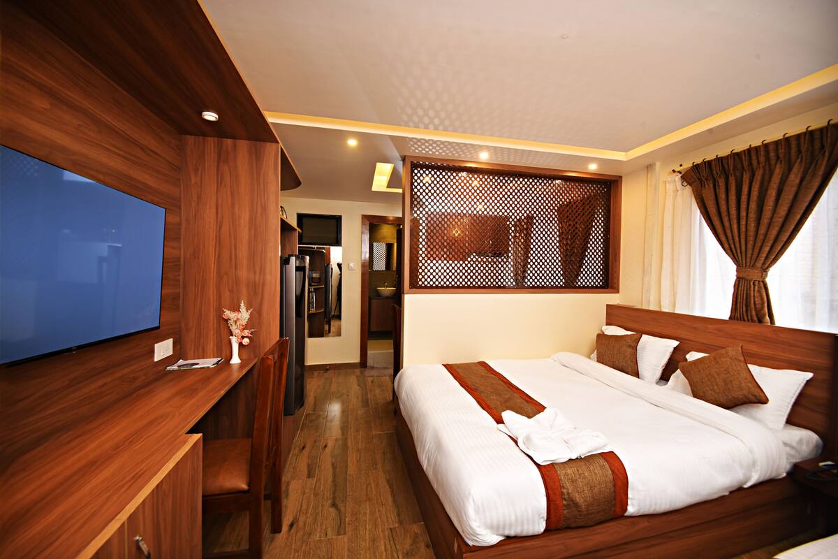 A hotel room with a wooden bed, a TV, a desk, and a bathroom visible through an open door.