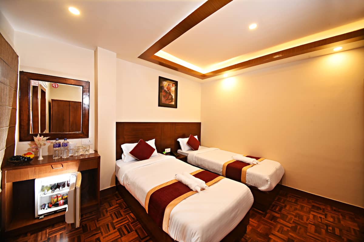 A hotel room with two beds, a minibar, a wooden desk, and a mirror.